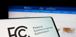 Close-up of a mobile device displaying the FCC logo with a website in the background