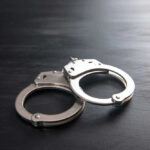 SHOCKING Arrest Figures: Operation Midway Blitz Metal handcuffs on a dark textured surface.
