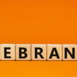 SHOCK Logo Swap: Goodbye, Fish! Wooden blocks spelling the word REBRAND on an orange background