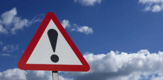 Warning sign with exclamation mark against sky