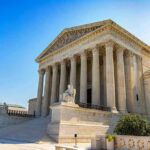 Stone building with columns and statues, clear blue sky.