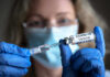 Person with gloves holding COVID-19 vaccine syringe.