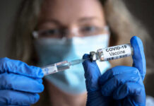 Person with gloves holding COVID-19 vaccine syringe.