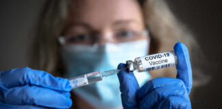Person with gloves holding COVID-19 vaccine syringe.