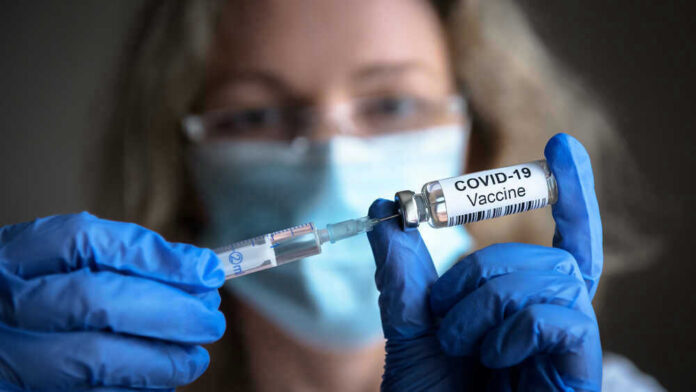 Person with gloves holding COVID-19 vaccine syringe.