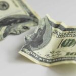 Torn and crumpled hundred dollar bills on a white surface