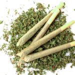 Three rolled cannabis joints on a bed of loose cannabis leaves