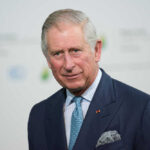 King Charles in a suit and tie smiling.