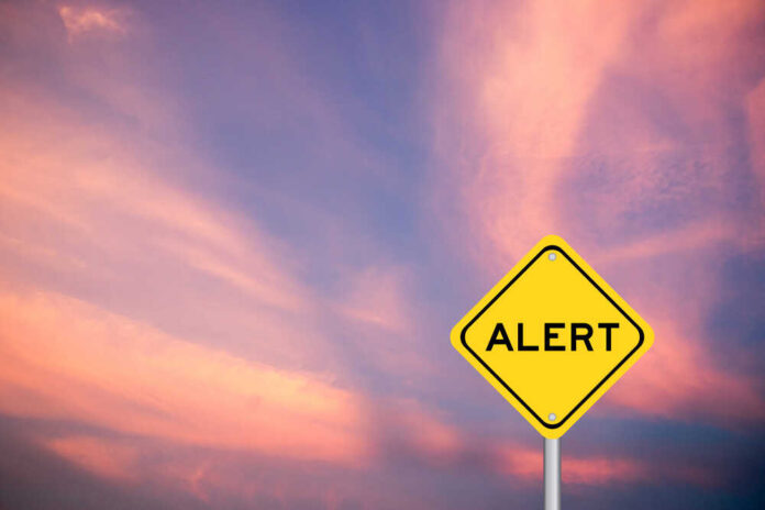 shutterstock_1814257538.jpg Yellow alert sign against a colorful sunset sky