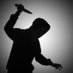 Silhouette of hooded figure holding a knife.