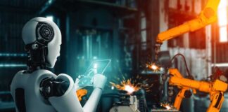 A humanoid robot using a tablet in an industrial setting with robotic arms in action