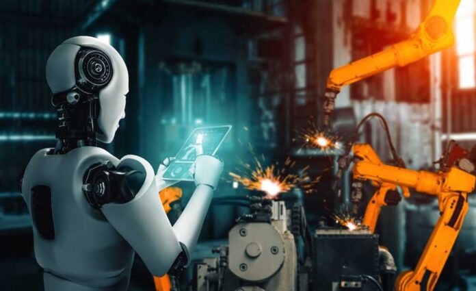 shutterstock_2474247487.jpg A humanoid robot using a tablet in an industrial setting with robotic arms in action