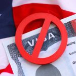 A red 'no' symbol over a visa document on an American flag background