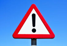 A triangular warning sign with an exclamation mark against a blue sky