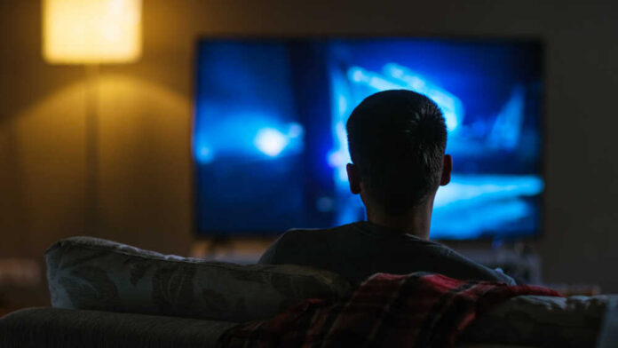 Person sitting on a couch watching a television screen in a dimly lit room