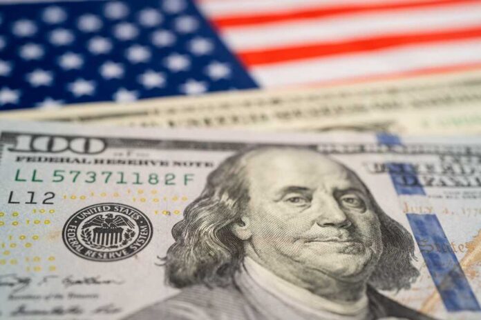 Close-up of a hundred dollar bill in front of an American flag
