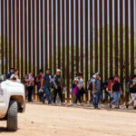 Group of people walking by a border fence.
