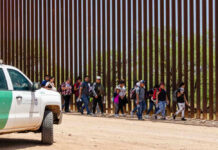 Hidden Illegal Count Dwarfs Estimates Group of people walking by a border fence.