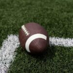 A brown football resting on green artificial turf near a white line