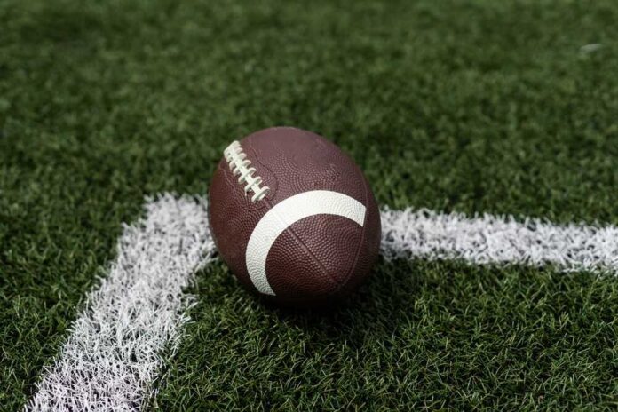 A brown football resting on green artificial turf near a white line