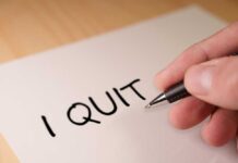 A hand writing 'I QUIT' on a piece of paper