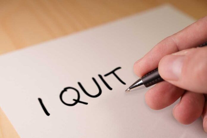 A hand writing 'I QUIT' on a piece of paper