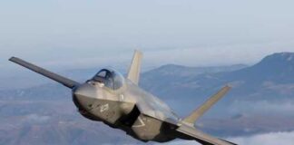 F-35 fighter jet flying above clouds with mountains in the background
