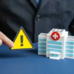 A business professional holding a warning sign next to a model of a hospital