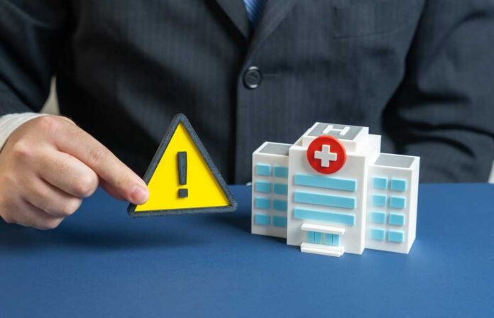 A business professional holding a warning sign next to a model of a hospital