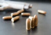 Close-up of bullets on a dark surface with a handgun in the background