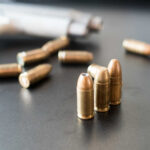 Close-up of bullets on a dark surface with a handgun in the background