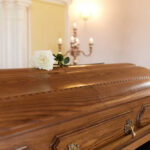A wooden casket with a white rose placed on top in a solemn setting