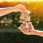 Hands exchanging burlap money bags outdoors.