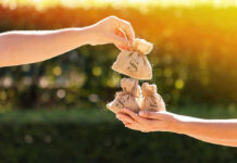Hands exchanging burlap money bags outdoors.