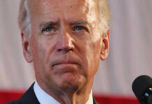 Biden’s Protector Shoots Himself at Airport Man speaking in front of a microphone.