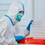 Healthcare worker in protective gear disposing of waste
