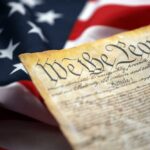 Close-up of a historical document with the American flag in the background