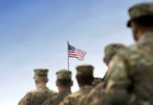 Soldiers in uniform with American flag in background.