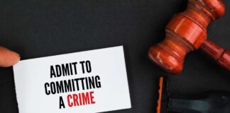 A hand holding a card that says 'ADMIT TO COMMITTING A CRIME' next to a gavel and a shaving razor