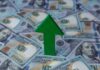 Green arrow pointing upwards on a background of hundred dollar bills