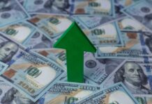 Green arrow pointing upwards on a background of hundred dollar bills