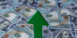 Green arrow pointing upwards on a background of hundred dollar bills