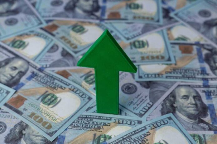 Green arrow pointing upwards on a background of hundred dollar bills