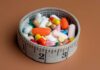 Weight-Loss Meds HALVED — Trump’s Move Succeeds A bowl filled with various colorful pills and capsules next to a measuring tape