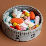 A bowl filled with various colorful pills and capsules next to a measuring tape