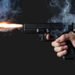 A hand holding a gun with smoke and a flash from the muzzle