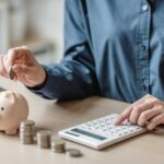 Families Borrowing Just to Buy Groceries Now?! Person placing a coin into a piggy bank while using a calculator