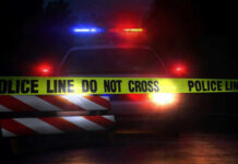 Horrorific Crime Scene: 3 Dead, Many More Injured Police car with flashing lights behind caution tape.