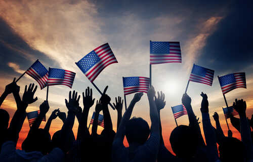 Group,Of,People,Waving,American,Flags,In,Back,Lit Silhouetted crowd holding American flags against a sunset