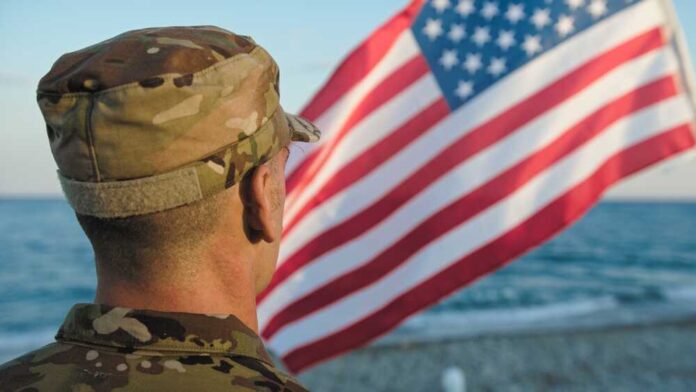 Military,Next,To,Flag,As,Patriotism,Concept Soldier in uniform standing in front of an American flag by the ocean